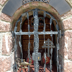 Schmiedeeisernes Denkmal der Heiligen mit Attributen auf dem Gitter. Feuergef und das libanesische Kreuz
