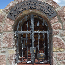 Schmiedeeisernes Denkmal der Heiligen mit Attributen auf dem Gitter. St. Franz von Assisi – Tau-Zeichen, St. Antonius von Padua – Brot