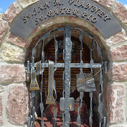 Kovaný památník svatých s atributy na mřížích. Sv. Ján M. Vianney - štola, Sv. Páter Pio - list s nápisem Pokání